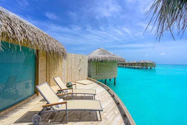 Sun loungers on the wooden deck of an overwater villa with thatched roof above a turquoise lagoon at You & Me