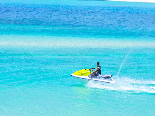 A rider on a yellow and white jet ski crosses turquoise lagoon water at You & Me Maldives, Raa