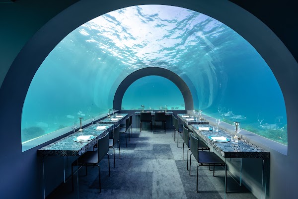Empty underwater restaurant with arched glass walls, set tables and blue ocean light at You & Me