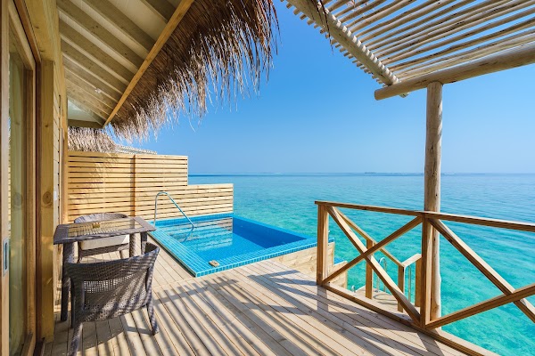 Overwater villa deck at You & Me Maldives with plunge pool, wicker seating and ladder into the turquoise lagoon under a