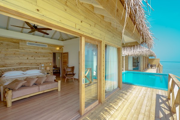 Overwater villa interior with wooden walls, private pool and thatched roof overlooking the lagoon at You & Me