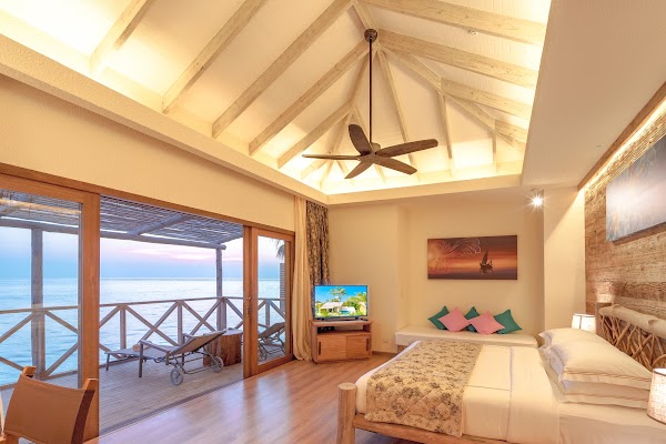 Overwater villa bedroom at You & Me Maldives with vaulted wooden ceiling, king bed and sea-facing deck at