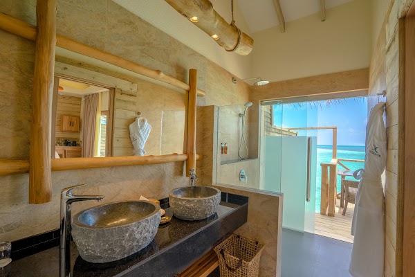 Bathroom interior at You & Me Maldives with twin stone basins, timber-framed mirror and open doors onto a lagoon-view