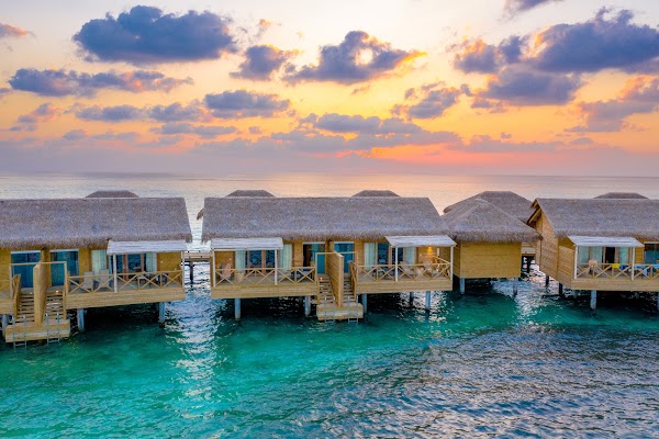 Thatched overwater villas at sunset above turquoise lagoon, You & Me Maldives, Raa Atoll, aerial