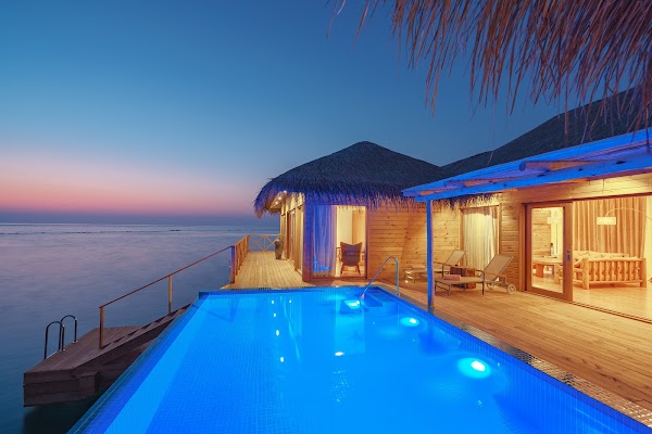 Overwater villa with lit private pool and deck at dusk, You & Me Maldives, Raa