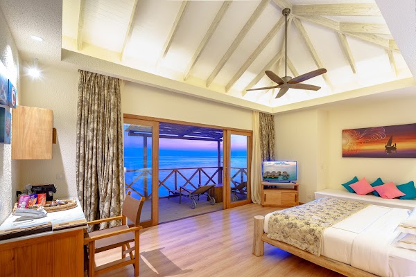 Overwater villa bedroom at You & Me Maldives with vaulted ceiling, wooden bed and doors open to a twilight