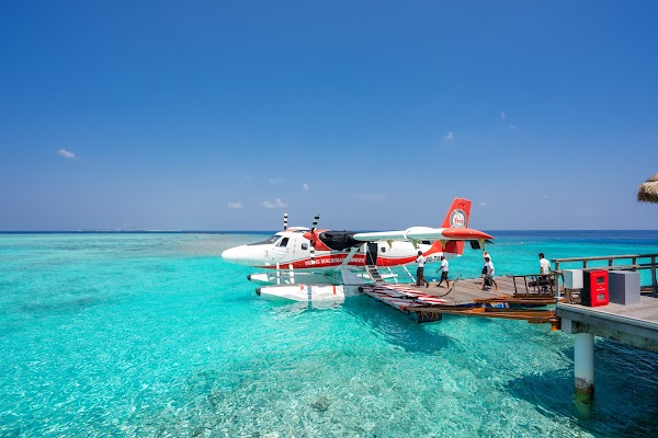 Seaplane moored beside a wooden jetty in a turquoise lagoon as passengers with luggage board under a clear blue