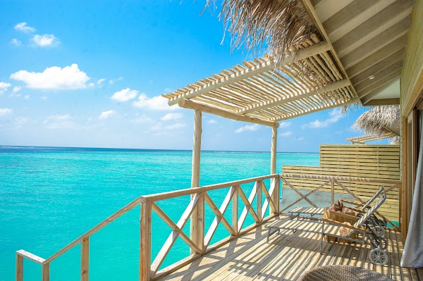 Wooden deck of an overwater villa with sun loungers and thatched pergola overlooking a turquoise lagoon at You & Me